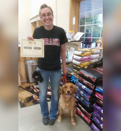 Golden Retriever sitting beside woman standing with a certificate in hand